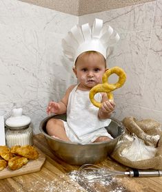 a baby sitting in a bowl holding a pretzel