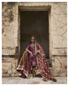 a woman in a purple and gold bridal outfit sitting on a stone floor next to a window