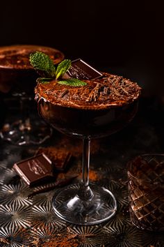 two chocolate martinis with mint garnish and chocolate bars on the rim, sitting on a patterned tablecloth