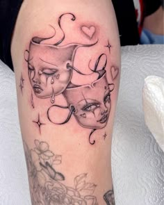 a woman's leg with tattoos on it and an image of two masks in the middle