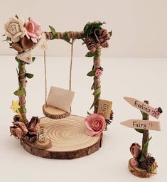 there is a miniature swing made out of wood and flowers on the tree stumps