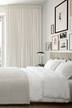 a white bed sitting in a bedroom next to a window with pictures on the wall