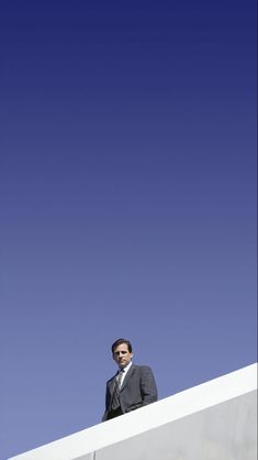 a man in a suit and tie standing on top of a white structure with a blue sky behind him