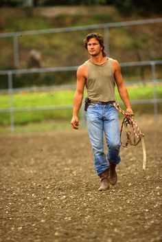 a man walking across a dirt field holding a cow's head in his hand