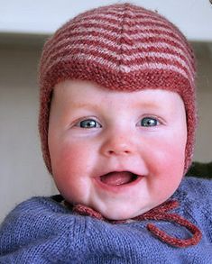 a baby wearing a knitted hat and smiling at the camera while being held by a woman