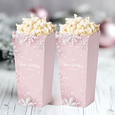 two pink paper bags filled with popcorn on top of a table