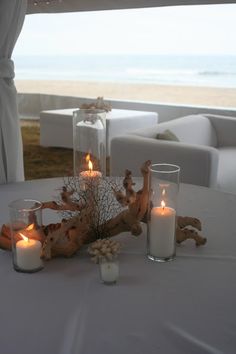 two candles are sitting on a table next to some glass vases and driftwood