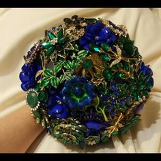 a blue and green brooch sitting on top of a white cloth next to a person's hand