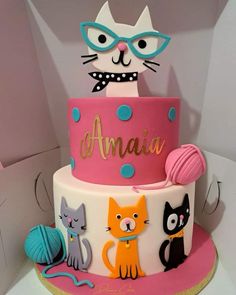 a birthday cake decorated with cats and balls of yarn on the top tier is pink, white, and blue