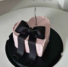 a pink and black heart shaped cake with a bow on the top sitting on a plate