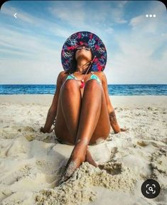 a woman sitting in the sand at the beach wearing a sunhat on her head