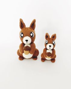 two small stuffed animals sitting next to each other on a white surface and one is wearing a brown knitted sweater