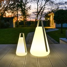 two white lamps sitting on top of a wooden table in front of a house at night