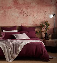 a bed with red sheets and pillows in front of a pink painted wall behind it