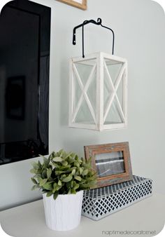 a white lantern hanging on the wall next to a potted plant and framed photograph