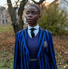 a woman wearing a blue and black striped suit standing in front of a tree with leaves