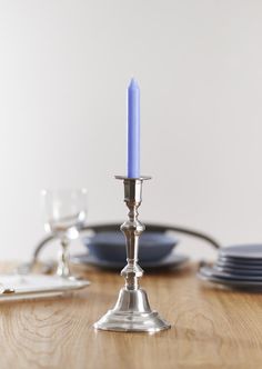 a blue candle is on top of a wooden table with plates and silverware in the background