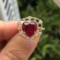 a woman's hand holding a ring with a heart shaped red stone in it