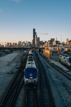 a blue and white train traveling through a city next to tall buildings on railroad tracks