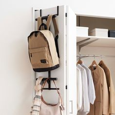 an open closet with clothes and bags hanging on the door handle, in front of a white wall