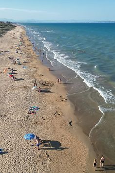 the beach is crowded with people and umbrellas as they walk along the water's edge