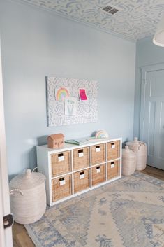 a baby's room with blue walls and white furniture, including baskets on the floor