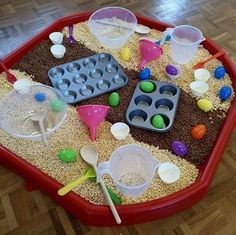 a red tray filled with sand and plastic utensils on top of a wooden floor