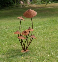 a metal sculpture in the shape of three mushrooms on top of green grass with trees behind it