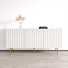 a white cabinet sitting on top of a wooden floor next to a vase with flowers