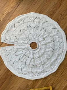 a white crocheted doily sitting on top of a wooden floor next to a ruler