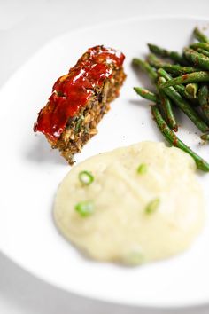 a white plate topped with green beans and meat next to mashed potatoes on a table