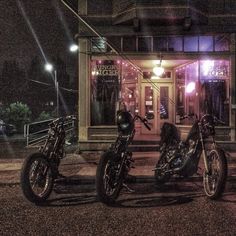 two motorcycles are parked in front of a building at night with lights on the windows