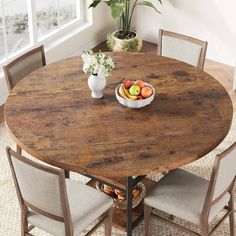 a wooden table with four chairs around it and fruit on the plate at the center