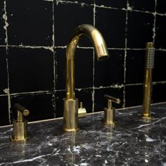 two gold faucets are sitting on a marble countertop in front of black tiles