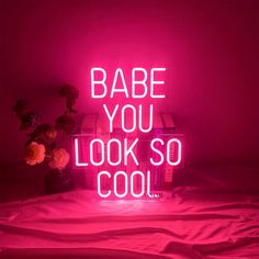 a neon sign that says babe you look so cool on a bed with pink sheets