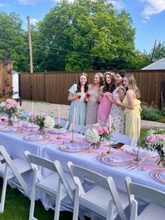 a group of girls standing around a table with flowers and candles on it in front of a fence