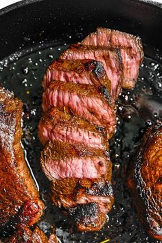 three steaks cooking in a skillet with oil