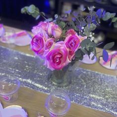 a vase filled with pink roses sitting on top of a table next to plates and cups