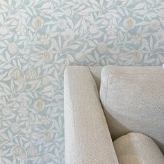 a white chair sitting in front of a wallpapered wall with leaves on it