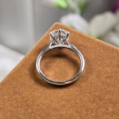 a diamond ring sitting on top of a brown velvet box with flowers in the background