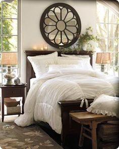 a bed with white comforter and pillows in front of a large round mirror on the wall