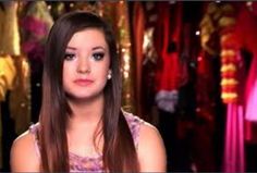 a woman with long brown hair is looking at the camera while wearing a purple dress