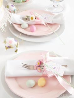 a table set for easter with pink plates and napkins, decorated eggs and flowers