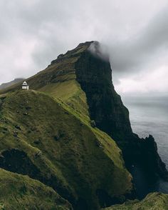 a house on the top of a mountain with fog in the air and water below