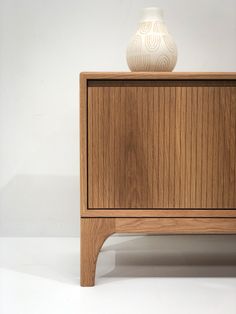 a white vase sitting on top of a wooden cabinet