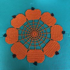 an orange crocheted doily on a blue background with black pins in the center