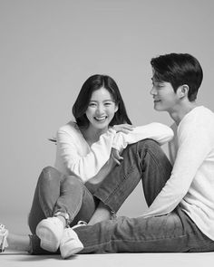 a young man and woman sitting on the floor smiling at each other while they both look into one another's eyes