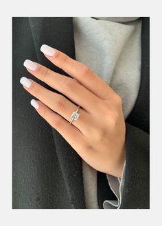 a woman's hand wearing a ring with a diamond in the middle and white nails