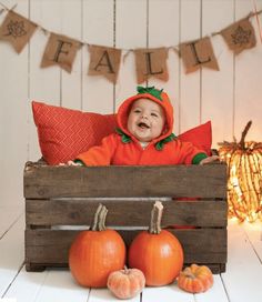 a baby is sitting in a crate with pumpkins on the floor and decorations around him