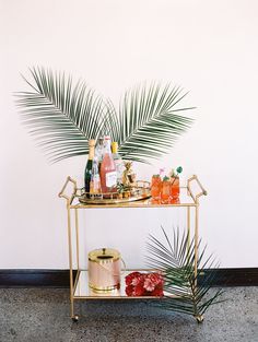 a gold bar cart with drinks on it and palm fronds next to it